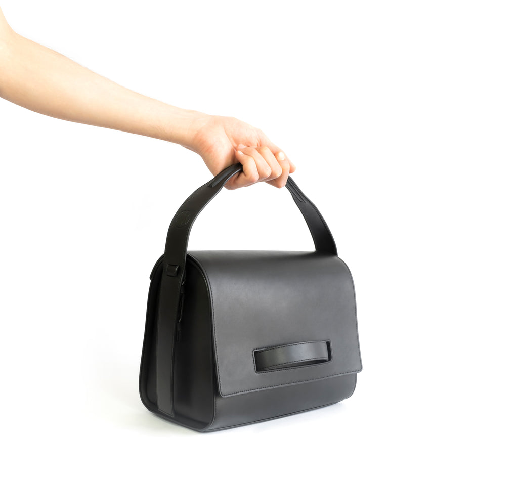 Black eco vegan leather barrel shoulder bag by Sydney Brown. Timeless, classic and modern. Hand view.