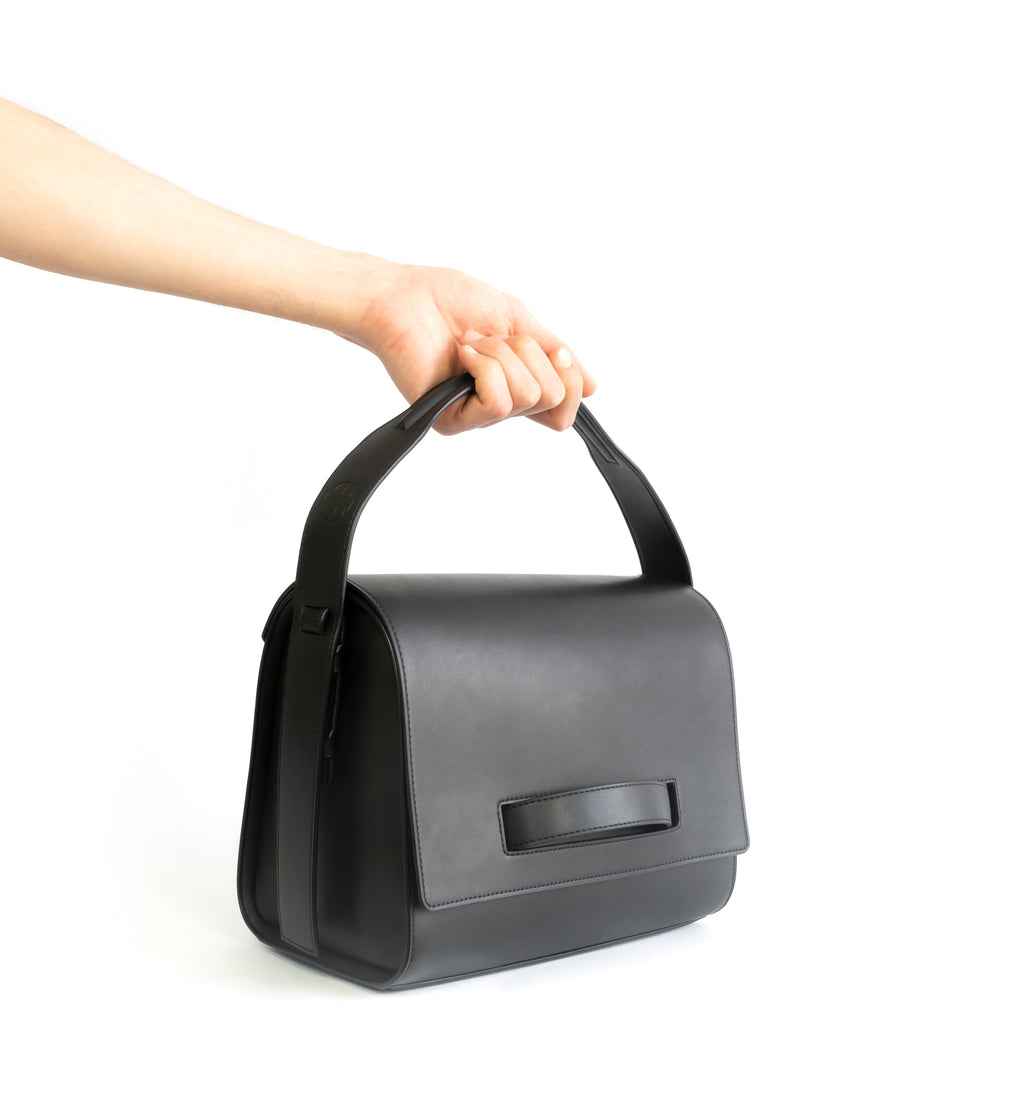 Black eco vegan leather barrel shoulder bag by Sydney Brown. Timeless, classic and modern. Hand view.