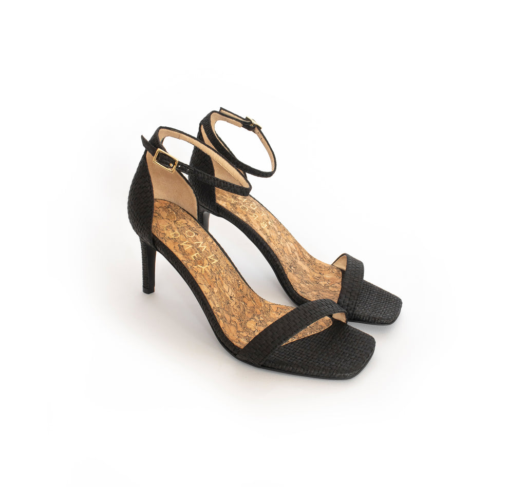 Low Stiletto in Black Raffia, ankle strap with metal buckle. Mid-heel in recycled wood pulp, covered with black raffia.