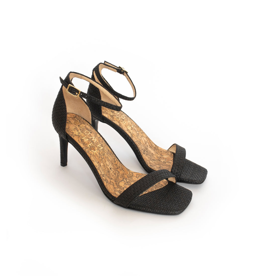 Low Stiletto in Black Raffia, ankle strap with metal buckle. Mid-heel in recycled wood pulp, covered with black raffia.