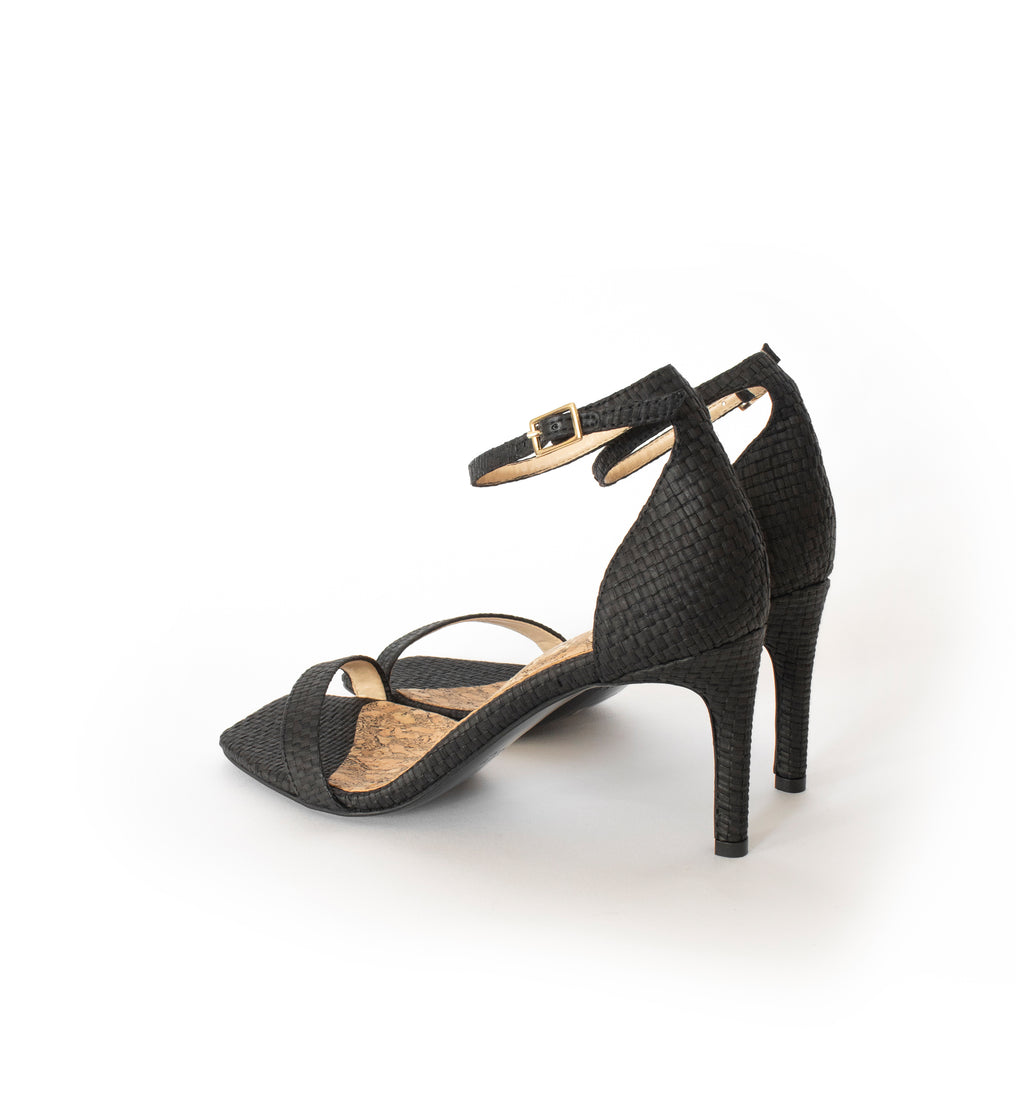 Low Stiletto in Black Raffia, ankle strap with metal buckle. Mid-heel in recycled wood pulp, covered with black raffia.