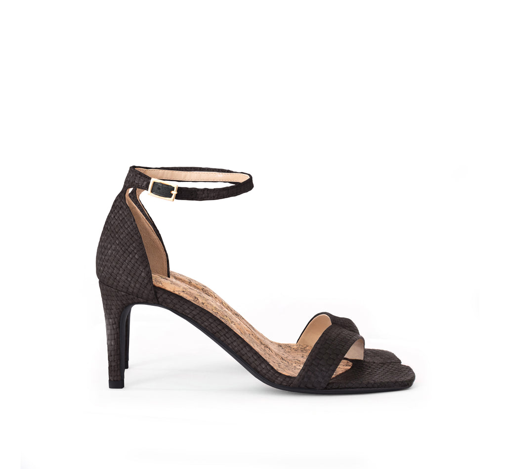 Low Stiletto in Black Raffia, ankle strap with metal buckle. Mid-heel in recycled wood pulp, covered with black raffia.