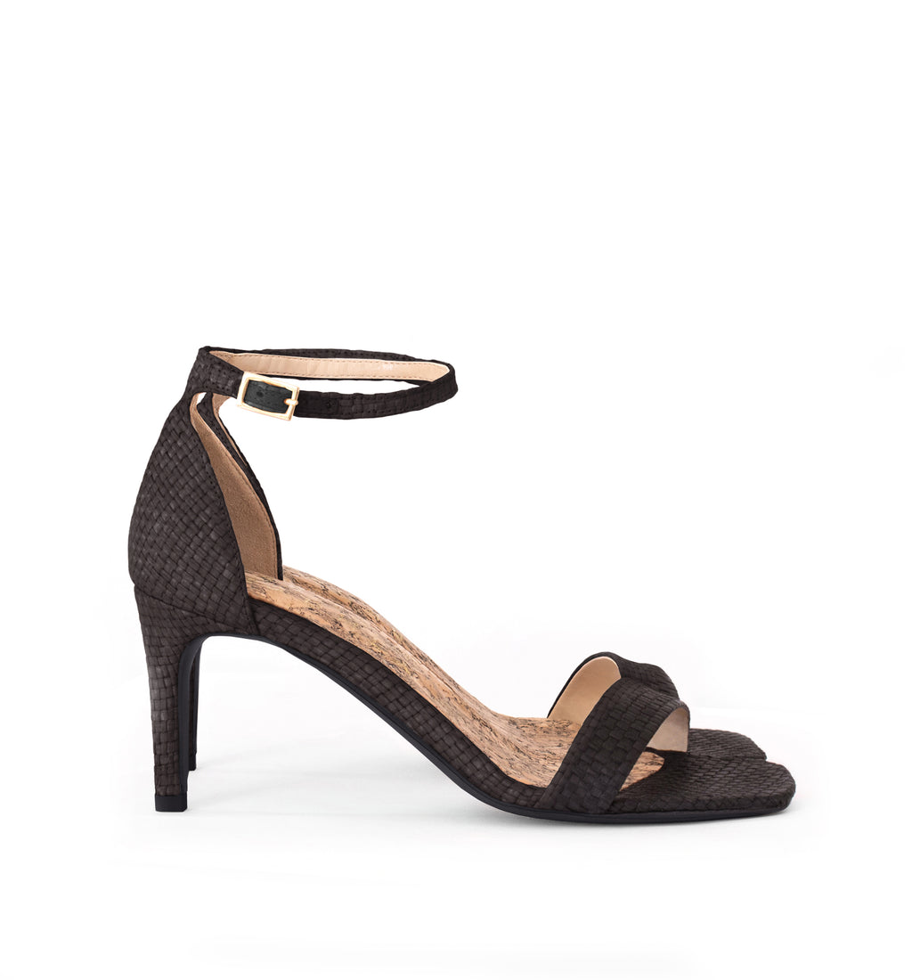 Low Stiletto in Black Raffia, ankle strap with metal buckle. Mid-heel in recycled wood pulp, covered with black raffia.