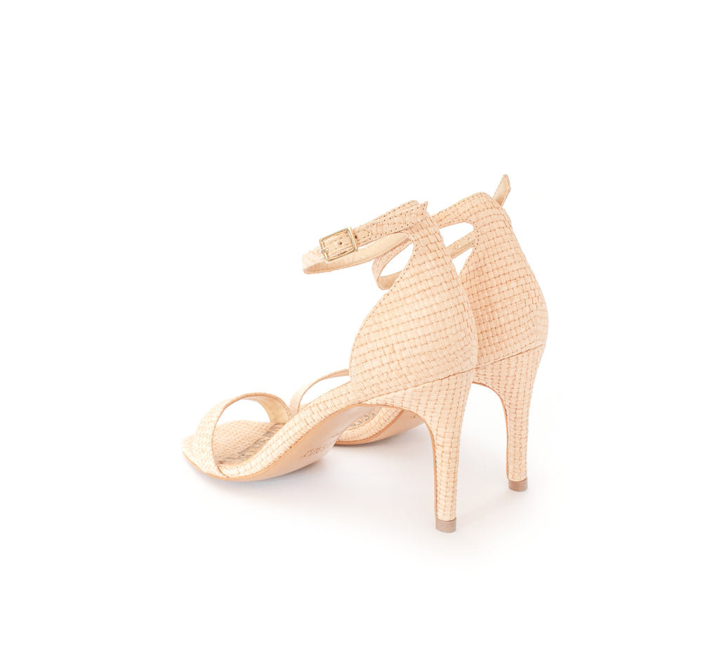 Low Stiletto in natural raffia, ankle strap with metal buckle. Mid-heel in recycled wood pulp, covered with natural raffia.